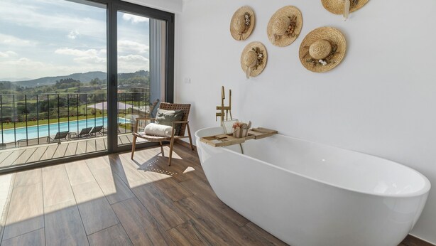 Un baño moderno con una bañera independiente, una silla de madera y vistas a una piscina.