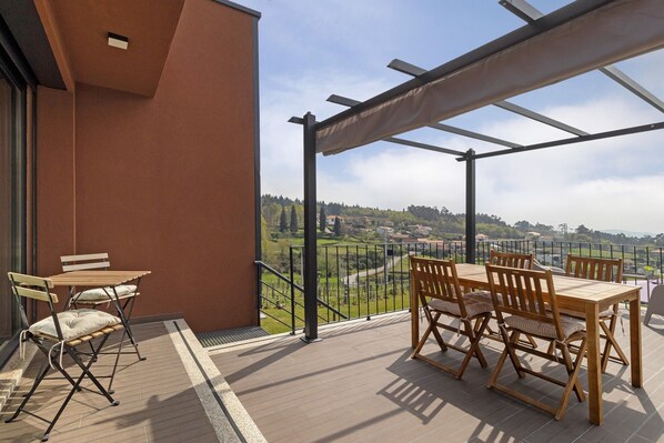Un balcón con mesa y sillas de madera, vista a un paisaje verde y cielo despejado.