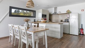 Una cocina moderna con armarios blancos, una mesa de comedor de madera y vistas a árboles a través de una ventana.