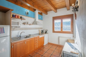 Una cocina con armarios de madera, microondas, pileta y ventana con vista a las montañas.