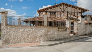 A stone building with a tiled roof, a metal fence, and a clear sky. - Rural House 'El Pico Llanillo' in Ribera del Duero with Private Pool (SAN MIGUEL DEL ARROYO)