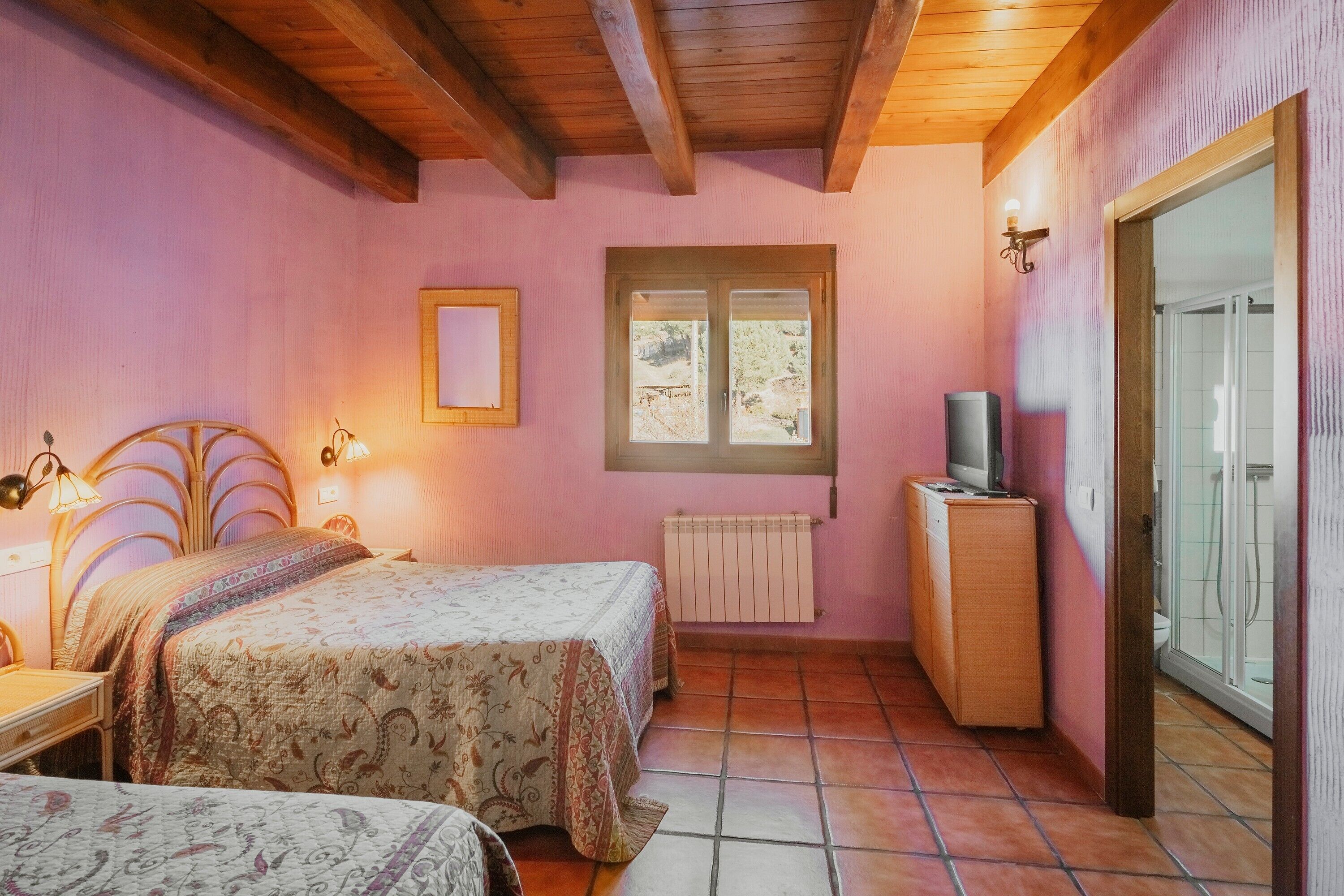 Een slaapkamer met twee bedden, een houten plafond, een raam, een radiator en een televisie.
