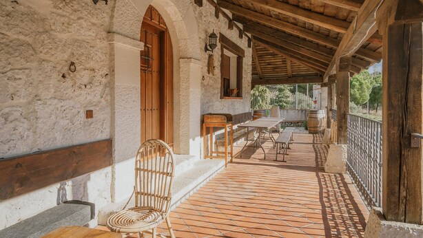 A covered outdoor area with a wooden bench, a wicker chair, and a table with chairs. - Rural House 'El Pico Llanillo' in Ribera del Duero with Private Pool (SAN MIGUEL DEL ARROYO)