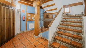 A hallway with a wooden door, a fire extinguisher, a blue wall, and a staircase with stone steps. - Rural House 'El Pico Llanillo' in Ribera del Duero with Private Pool (SAN MIGUEL DEL ARROYO)