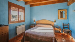 A bedroom with a wooden ceiling, a bed with a patterned bedspread, a nightstand, a chair, a dresser, and a window with blinds. - Rural House 'El Pico Llanillo' in Ribera del Duero with Private Pool (SAN MIGUEL DEL ARROYO)