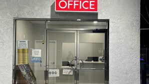 Entrada de hotel con puerta de vidrio, un cartel que dice 'NO REEMBOLSO', un cartel que dice 'USE LA OTRA PUERTA' y un cartel que dice 'OFICINA' sobre la puerta.