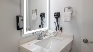 Un baño moderno con un espejo grande, un lavamanos, un secador de pelo y un perchero para toallas.