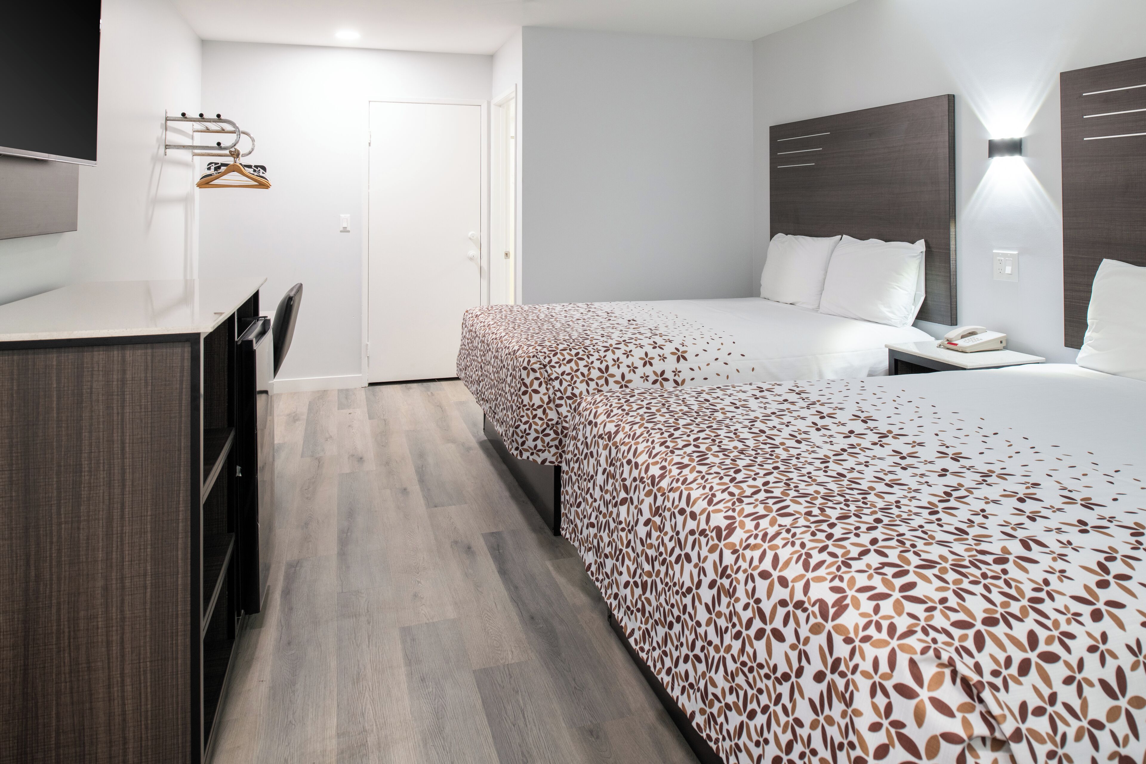 A hotel room with a bed, bedside table, and a desk with a chair.