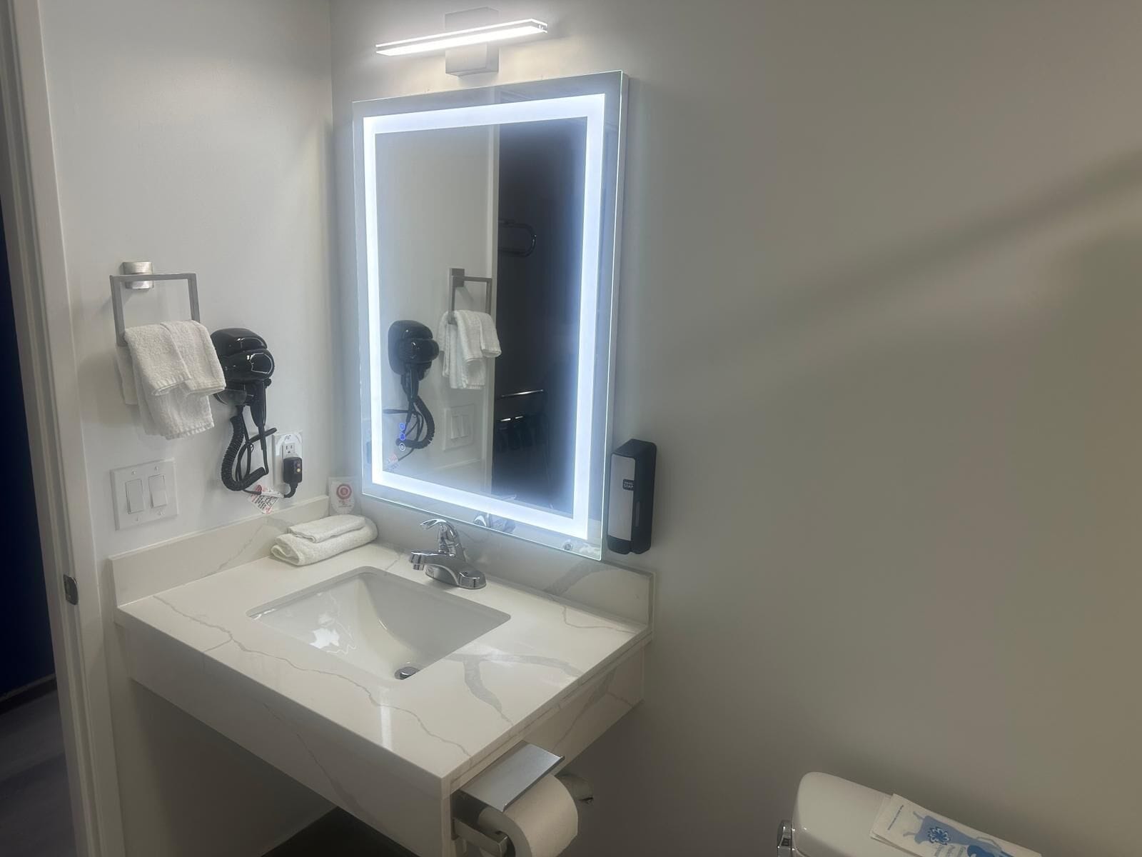 A modern bathroom with a large mirror, white sink, and a hairdryer on the wall.