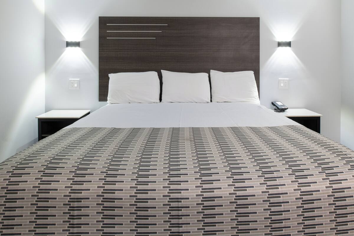 A modern hotel room with a large bed, a headboard with horizontal lines, two bedside tables, and wall-mounted lights.