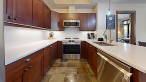 A kitchen with wooden cabinets, a stainless steel oven, a microwave, and a dishwasher. - Ski-In, Ski-Out 2-Bedroom Condo at Stone's Throw (Sun Peaks)