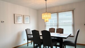 Un comedor con una mesa rectangular, seis sillas, una lámpara colgante y dos cuadros en la pared.