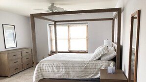 Un dormitorio con cama con dosel, una mesita de noche con lámpara, una ventana con persianas y un aparador.