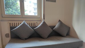A grey sofa with three cushions in a room with a radiator and a window. - Bèz Apartment in Milan Tortona street Fashion design district  (Milano)