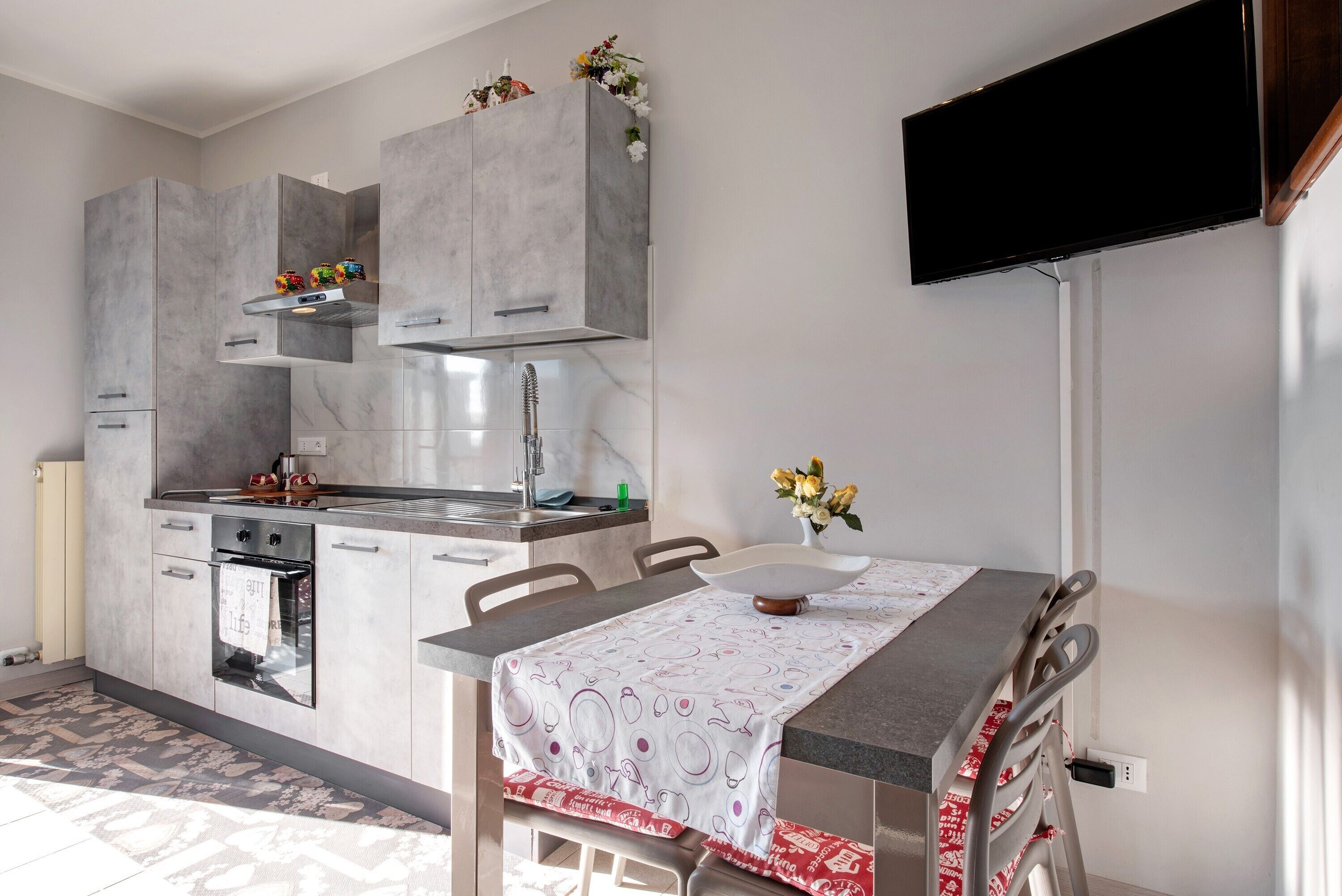 Une cuisine moderne avec des meubles gris, un four encastré et un coin repas comprenant une table et des chaises.