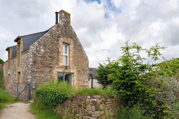 Una casa de piedra con techo inclinado, una chimenea visible y una entrada protegida por una reja.