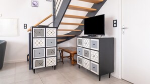 A staircase with wooden steps and a black railing, a black TV on a cabinet, and a small wooden bench. - Holiday Home 'La Longère Du Cosquer' with Private Terrace, Garden & Wi-Fi (Baden)