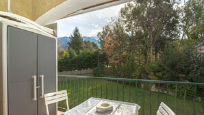 Un balcón con mesa y sillas, un armario gris y vistas a árboles y montañas.