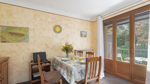 Un comedor con una mesa preparada para cuatro personas, una computadora portátil en un estante y vistas a través de un vidrio.