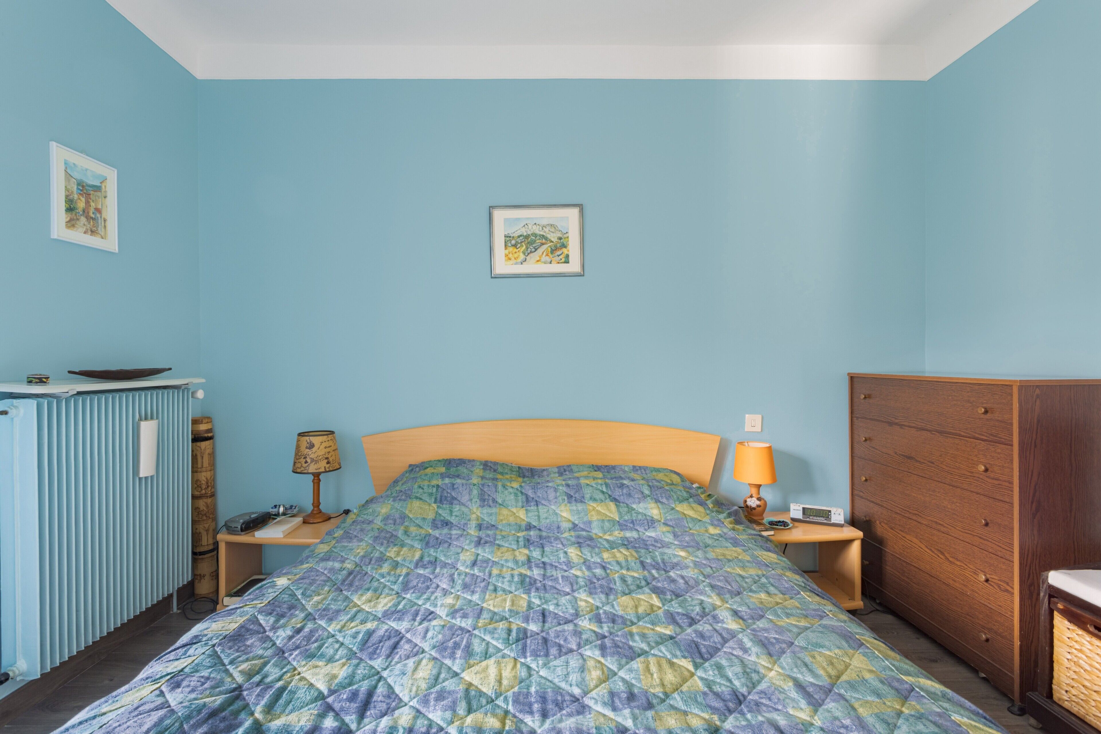 A bedroom with a bed, a dresser, a nightstand, a lamp, and a framed picture on the wall.
