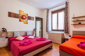 Ein Hotelzimmer mit zwei Betten, einem Fenster mit Vorhängen, einem Gemälde an der Wand und einem kleinen Regal mit einer Pflanze.