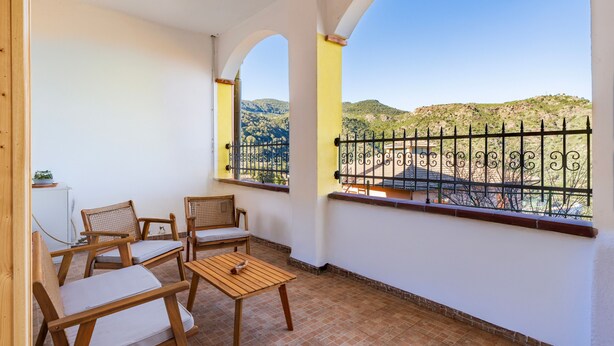 Un balcón con muebles de madera, vistas a colinas y barandilla de metal.