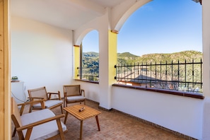 Un balcón con muebles de madera, vistas a colinas y barandilla de metal.