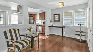 A spacious living area with a wooden floor, a striped armchair, a glass coffee table, and a kitchen in the background. - Stay in a charming 2-bedroom house in Omaha with WiFi, AC, and a peaceful vibe. (Omaha)