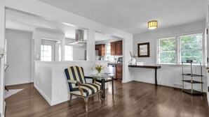 A spacious kitchen with wooden cabinets, a dining area with a striped chair, and a large window with greenery outside. - Stay in a charming 2-bedroom house in Omaha with WiFi, AC, and a peaceful vibe. (Omaha)