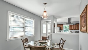 A dining area with a round glass table, four chairs, and a hanging light fixture. - Stay in a charming 2-bedroom house in Omaha with WiFi, AC, and a peaceful vibe. (Omaha)
