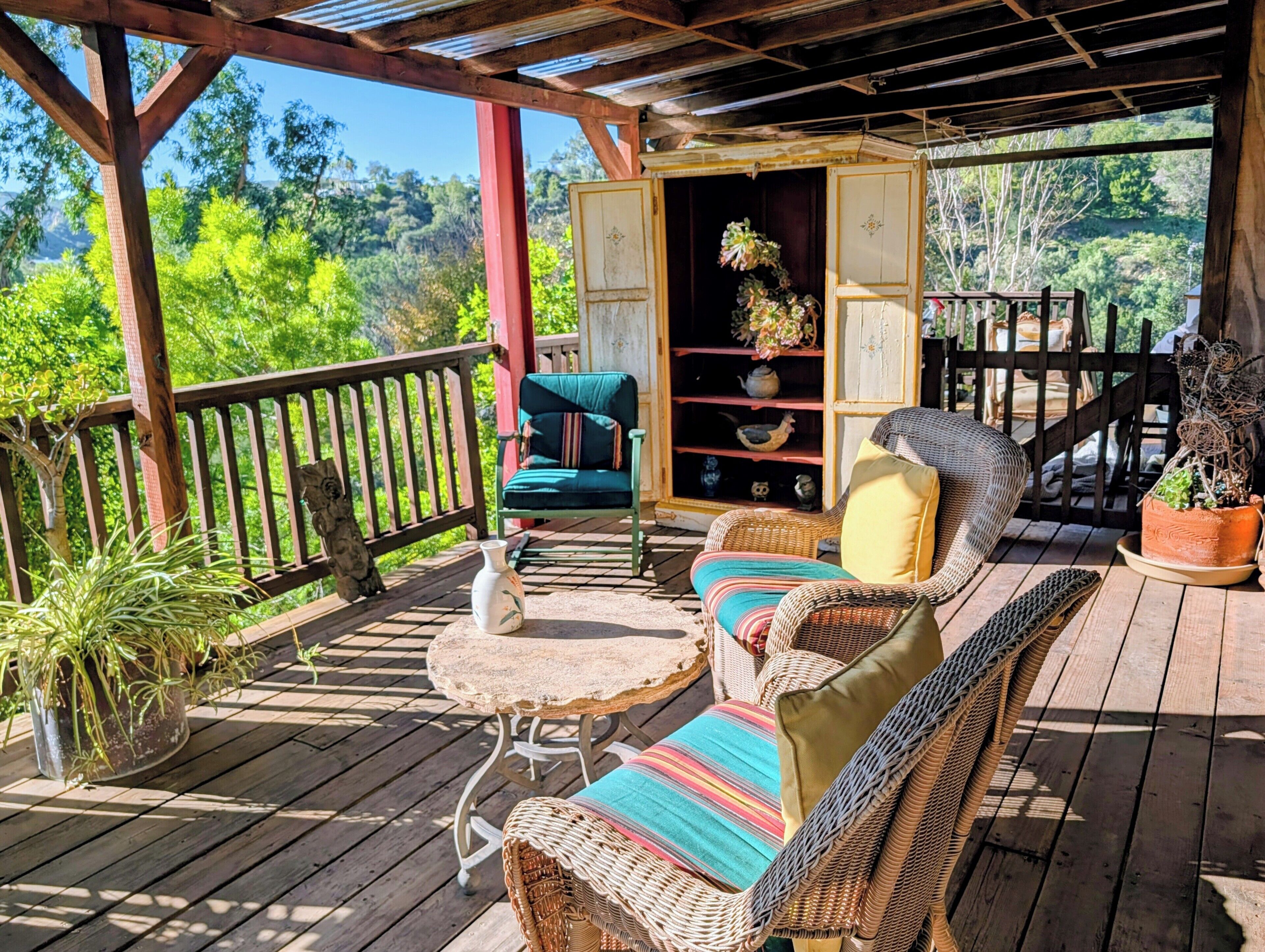 A wooden deck with wicker furniture, a stone table, and potted plants.