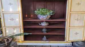 A wooden cabinet with a decorative top, a potted plant, and a teapot on the shelves. - European Style b&b in Topanga (Topanga)