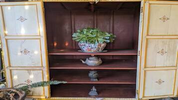 A wooden cabinet with a decorative top, a potted plant, and a teapot on the shelves.