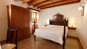 Une chambre à coucher avec un lit en bois, une armoire, une chaise et une table de chevet avec une lampe.