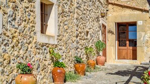 Un bâtiment en pierre avec une porte et des fenêtres en bois, des plantes en pot et un chemin pavé.