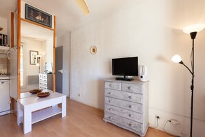 A room with a white table, a wooden dresser, a flat-screen TV, a lamp, and a ceiling fan.