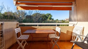 A balcony with a table and chairs, a view of trees and buildings, and a white railing.