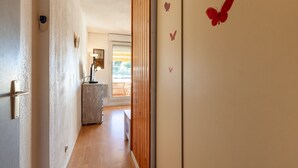 A hallway with a wooden door, a wall-mounted light fixture, and a window with blinds.