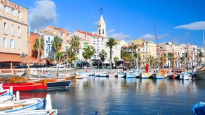 A marina with boats docked, a church with a bell tower, and colorful buildings along the waterfront.