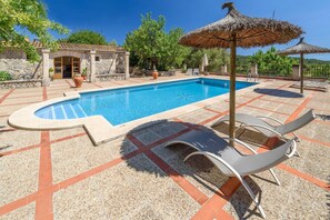 Ein Pool mit Liegestühlen und Sonnenschirmen, umgeben von Steinmauern und Grünpflanzen.