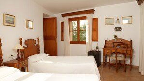 Une chambre avec deux lits, un bureau en bois, une chaise, une table de chevet, une lampe et une fenêtre avec des rideaux.