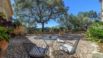 A patio with stone flooring, metal chairs, a round table, and a large tree providing shade.