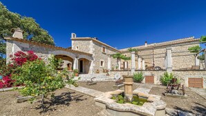 Un bâtiment en pierre doté d’une cour, d’une fontaine et d’une brouette.