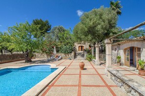 Un espace piscine doté d’une terrasse carrelée, d’un mur en pierre et d’une pergola.