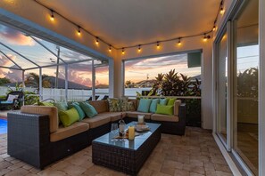 A covered outdoor seating area with a glass-top table, cushioned sofas, and string lights.