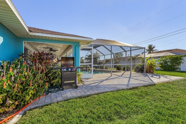 A backyard with a grill, a glass enclosure, and a swimming pool.
