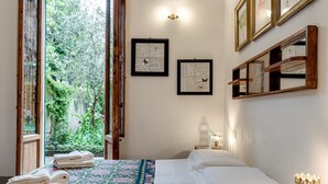 A hotel room with a bed, a window with a view of greenery, and wall-mounted artwork. - Apartment 'La Casa Vintage' with Private Garden, Wi-Fi and Air Conditioning (Firenze)