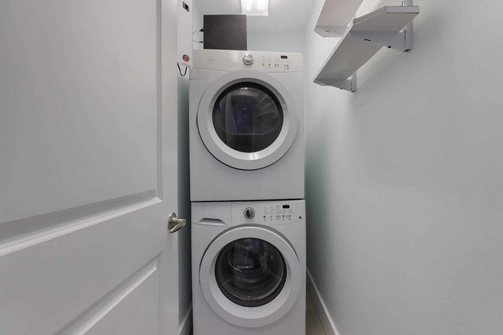 Une buanderie équipée de deux machines à laver à chargement frontal superposées, d’une bouche d’aération au-dessus de la machine du dessus et d’une porte blanche.