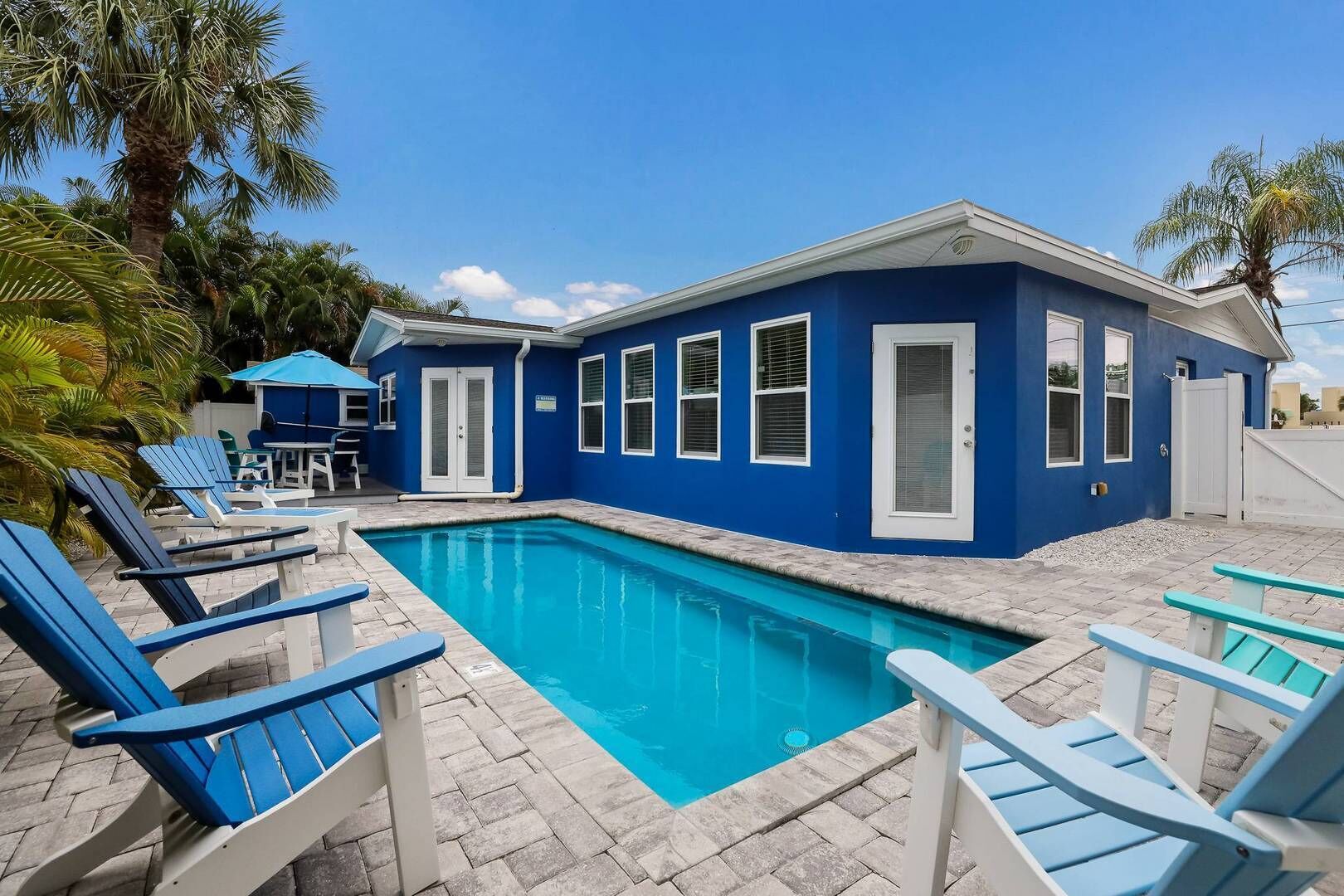 A blue house with a swimming pool, lounge chairs, and a patio area.