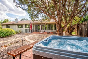 Un patio trasero con un jacuzzi, un banco de madera, un área de patio y un árbol grande.